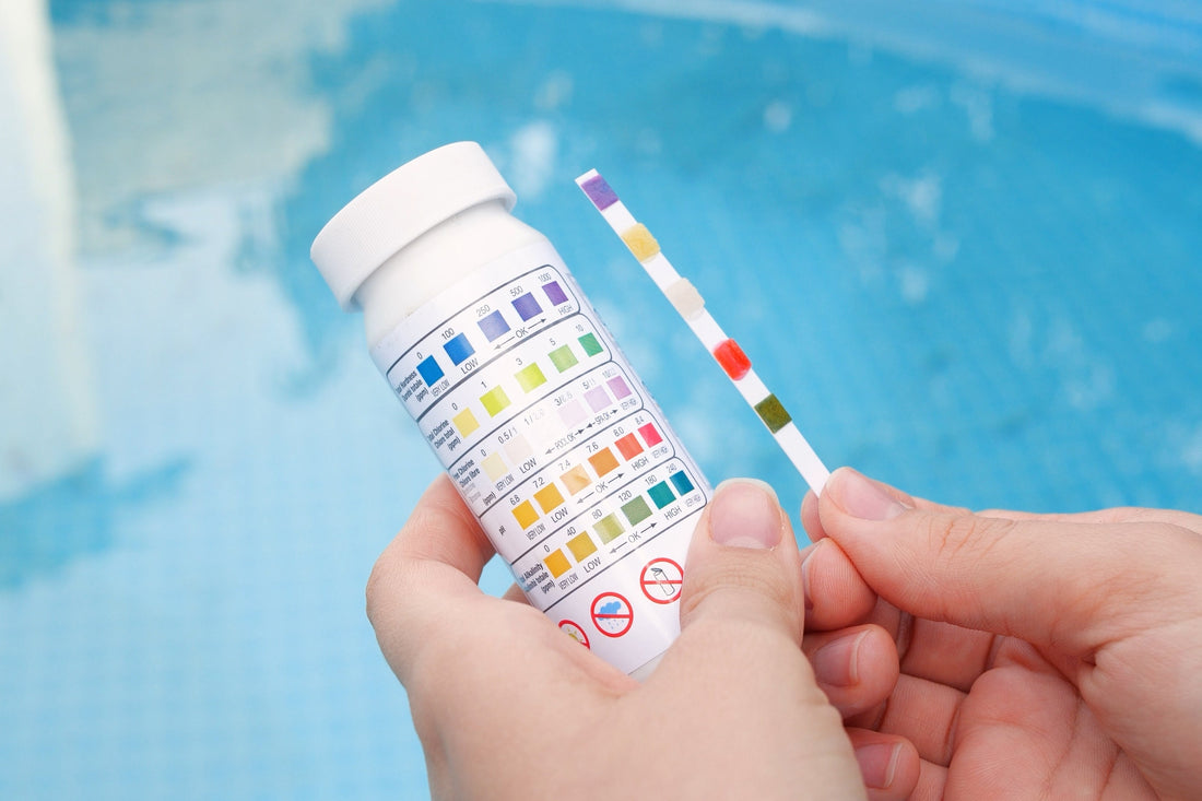 image of hands holding pool water test strip kit in front of a clear pool