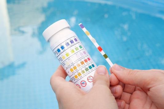 image of hands holding pool water test strip kit in front of a clear pool